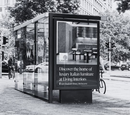 Modern black and glass bus shelter advertisement for Living Interiors luxury home furnishings on a city street